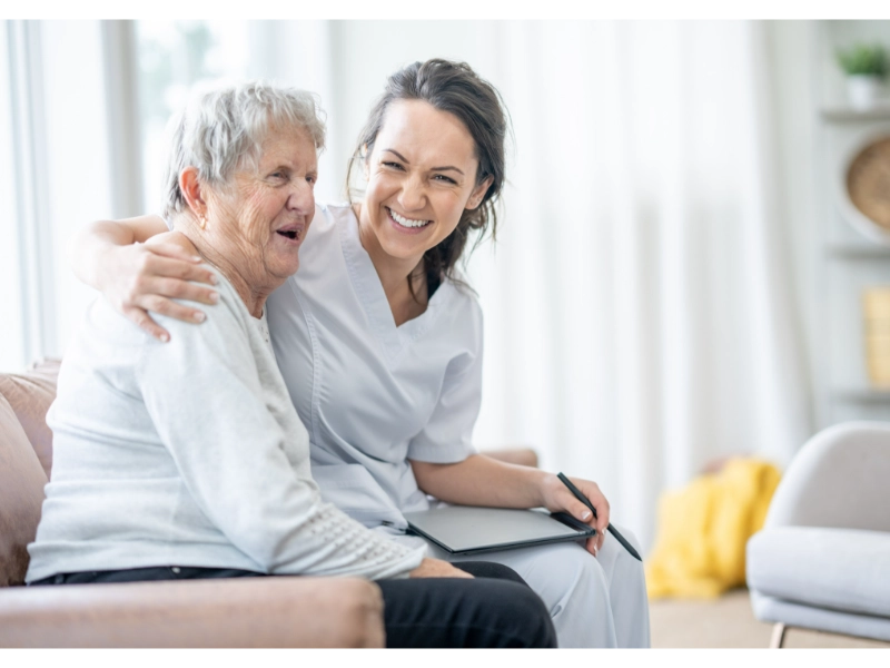 A smiling elderly couple sitting together in a bright home environment, symbolising companionship, care, and senior support.