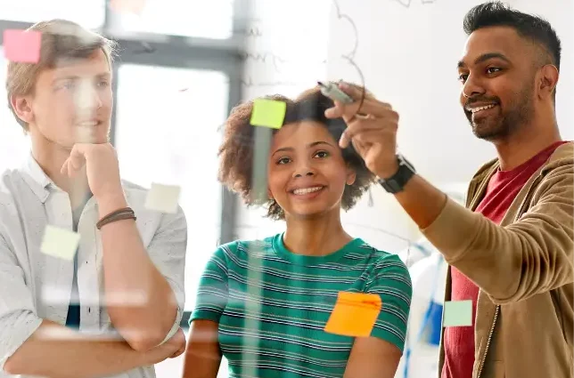 A group of young professionals engaged in a discussion, smiling and collaborating in a workplace setting, symbolising teamwork, diversity, and positive communication.